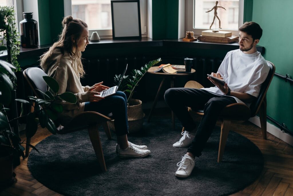 pexels-photo-4065133 A man and woman engaged in conversation at a stylish, plant-filled home office with modern furniture and digital devices.